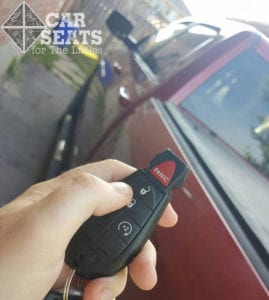 Lock before you leave: adult's hand pushing lock button on key in front of red truck