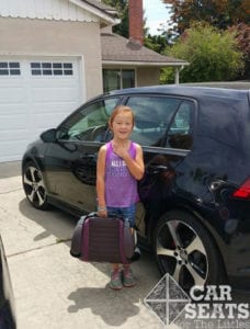 Chicco GoFit on the go: child standing in driveway next to black sedan holding GoFit booster by the handle