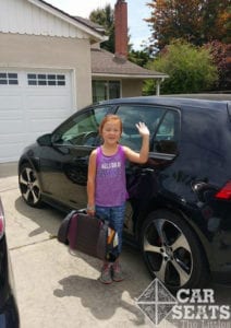 Driveway Safety: elementary aged child waving in driveway next to black sedan