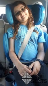Child properly buckled into teal booster seat